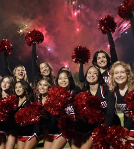 cheerleaders pose with fireworks overhead