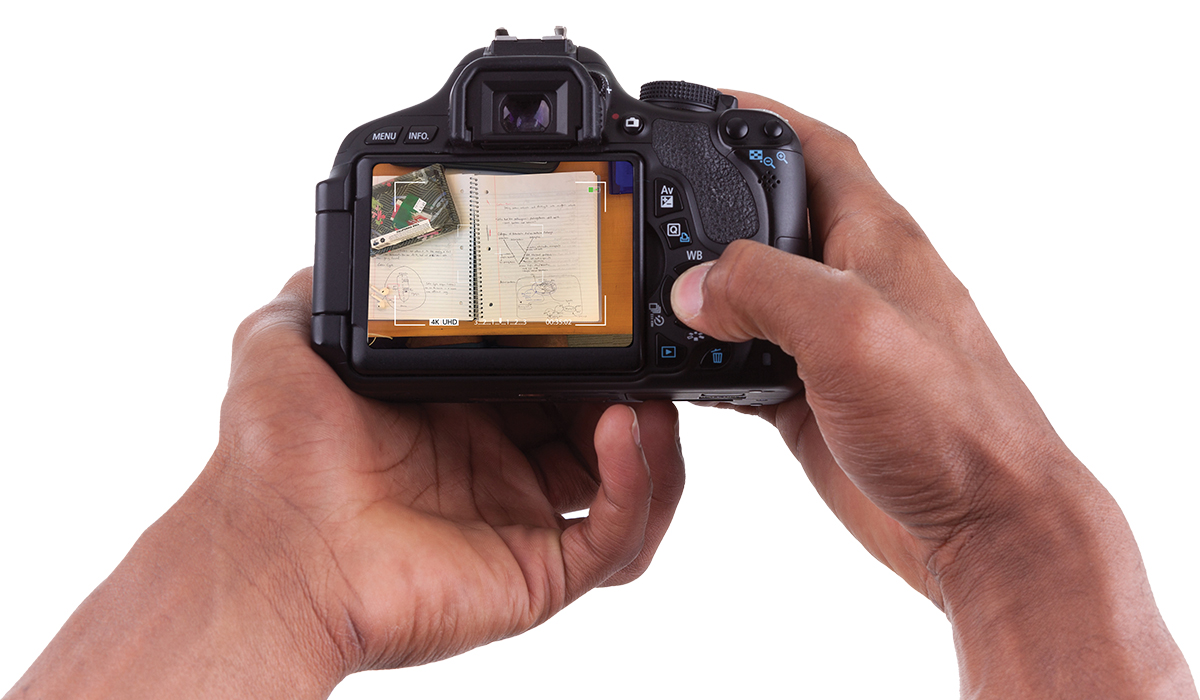 close up of hands holding a camera with a picture of a notebook seen on the viewscreen
