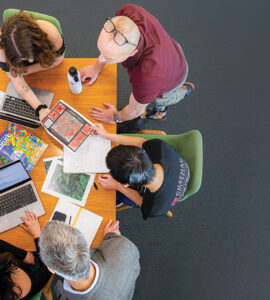 overhead shot of researchers gathered around table with copmuters, books and papers