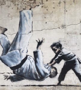 bansky artwork on a broken wall of child throwing down a male adult