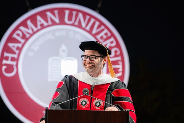 bill hader in academic gown with chapman university seal behind him