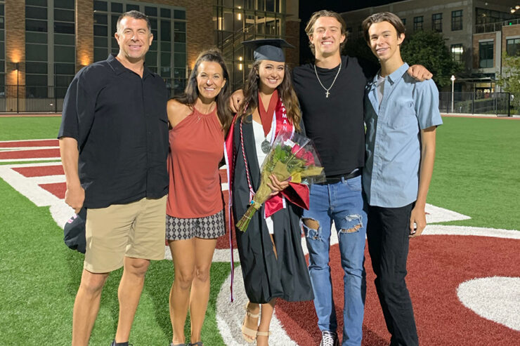 family of five on a stadium field, one child is wearing a graduation cap and gown