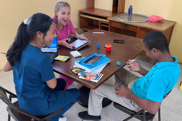 Chapman communication sciences and disorders students Adrienne Lee (MS '25) and Brooke Magill (MS '25) talk with a student in Dominica.