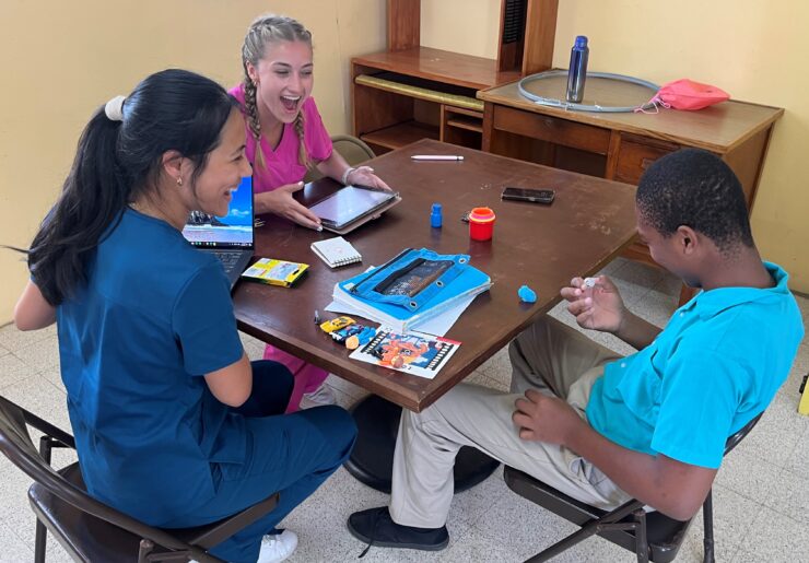 Chapman communication sciences and disorders students Adrienne Lee (MS '25) and Brooke Magill (MS '25) talk with a student in Dominica.