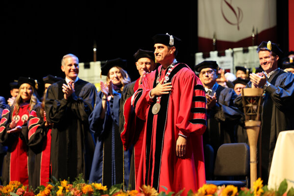 Matt Parlow in academic robes on stage with faculty etc