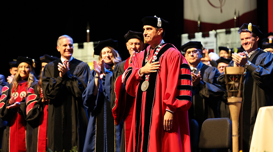 Matt Parlow in academic robes on stage with faculty etc
