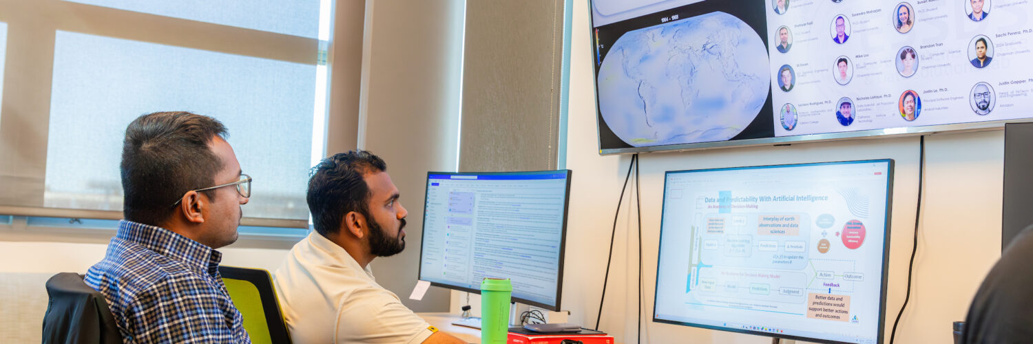 Two students work on multiple computer screens showcasing data and graphs of Earth.