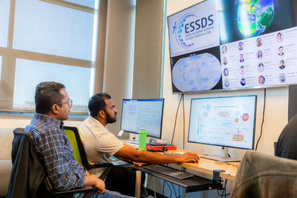 Two students work on multiple computer screens showcasing data and graphs of Earth.