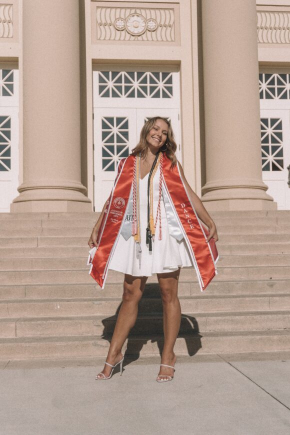 Natalie posing on the step of Memorial Auditorium in graduation regalia