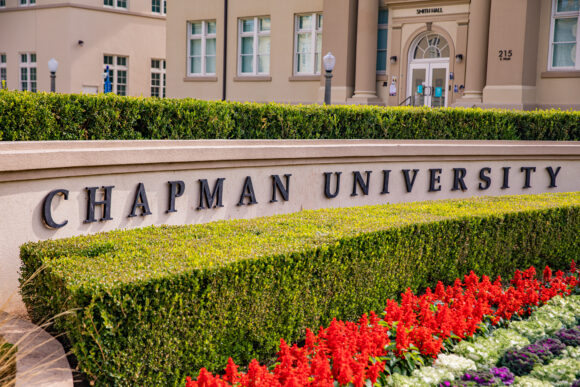 Chapman University sign in front of a landscaped campus building with trimmed hedges and red flowers.