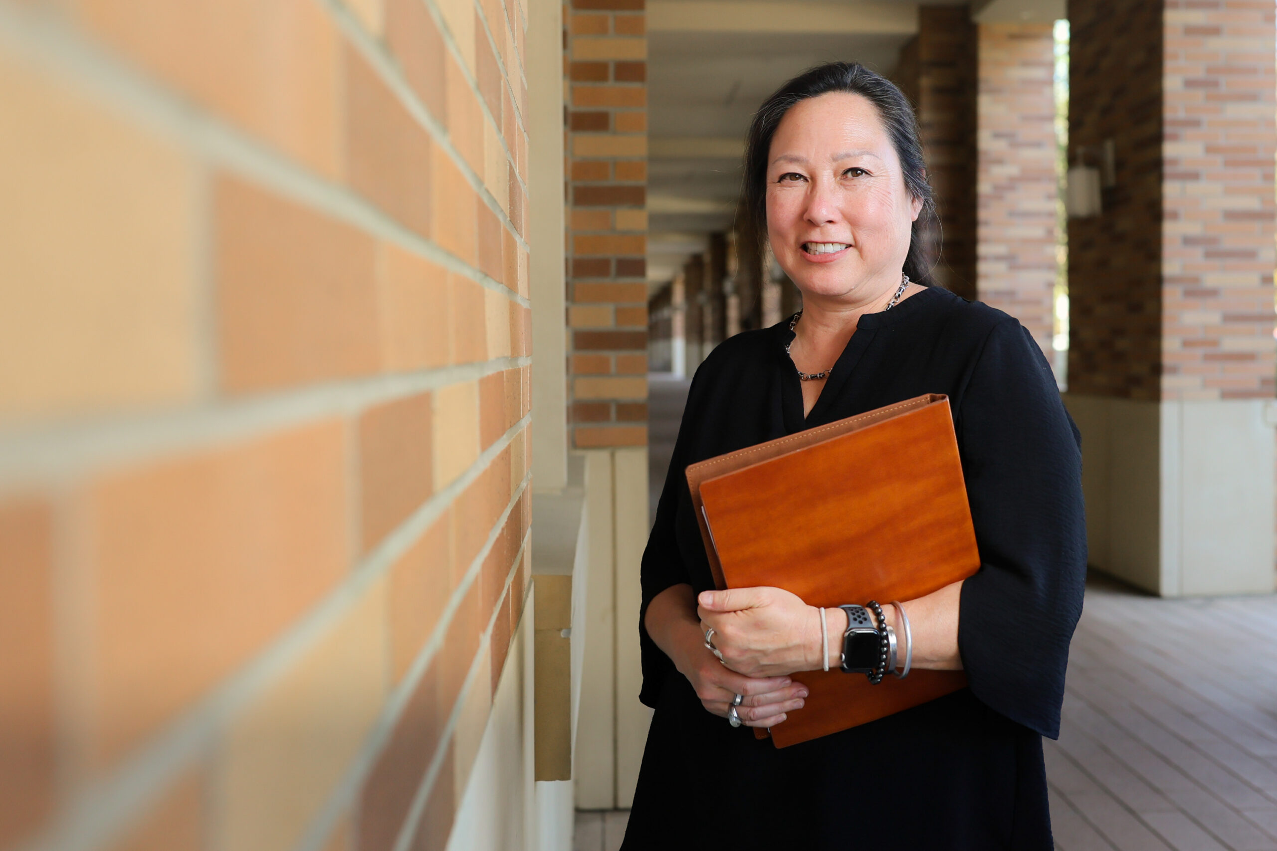 Stephanie Takaragawa, associate professor of sociology, stands next to a brick wall with folder in hand.
