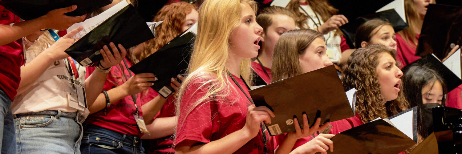 Students hold booklets as they sing on stage during a summer choral camp at Musco Center for the Arts.