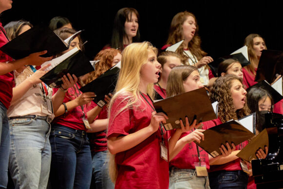 Students hold booklets as they sing on stage during a summer choral camp at Musco Center for the Arts.