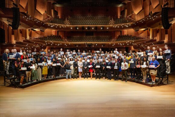 A large group of employer representatives pose for a photo onstage inside Musco Center for the Arts following a recognition ceremony at the State of the University.