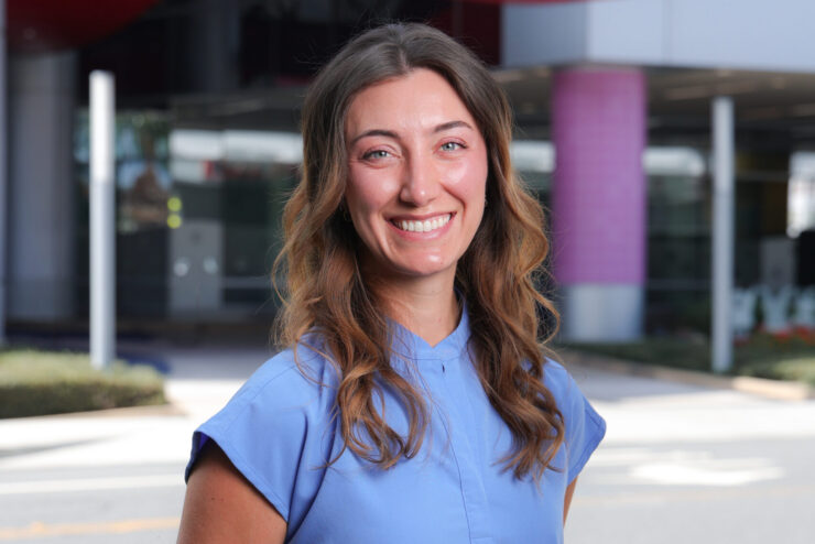 Erika Ebe stands outdoors in blue medical scrubs in front of the CHOC hospital sign.