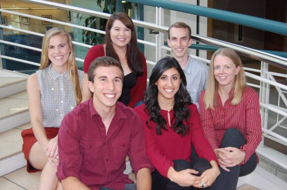Adam Kawali seated with a group of six college students on indoor steps, all smiling together.