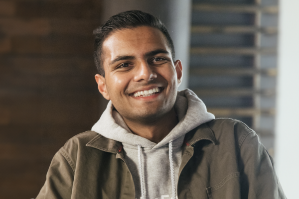 A portrait of a person wearing a jacket and hoodie, overlaid with a “Forbes Under 30 North America 2025” graphic.