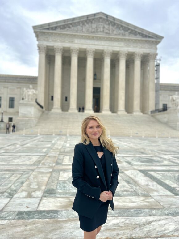 A person in a black blazer stands in front of the U.S. Supreme Court building on an overcast day.