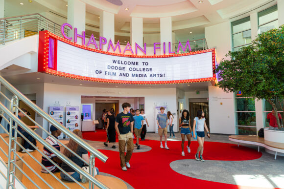 tudents walk through a bright lobby with a red carpet beneath a large “Chapman Film” marquee that reads “Welcome to Dodge College of Film and Media Arts.”