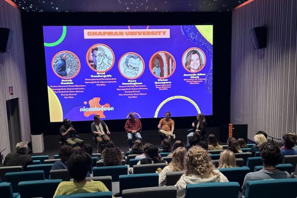 Auditorium view of students seated before a stage where five panelists sit under a large screen displaying a colorful Nickelodeon and Chapman University presentation slide.