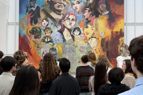 Crowd of people standing in front of a floor‑to‑ceiling mural filled with vibrant portraits and abstract shapes in warm reds, yellows and blues inside a white gallery space.