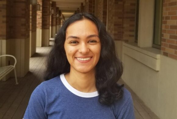 Arshia Sharma stands in a covered campus walkway lined with brick columns.