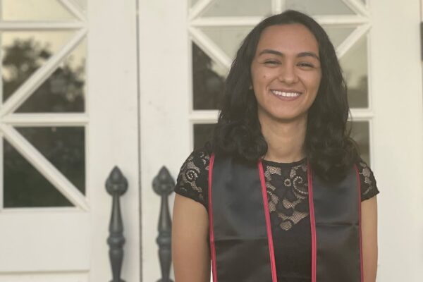 Arshia Sharma stands in front of white double doors wearing graduation regalia and a Chapman stole.