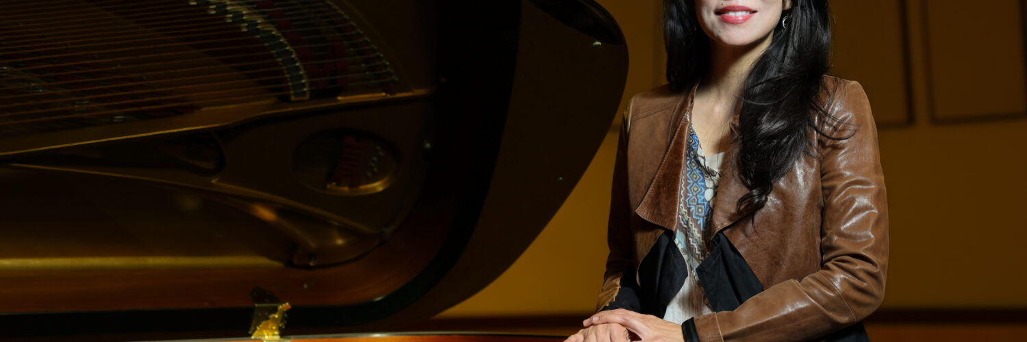 Grace Fong stands beside a grand piano in a performance hall.
