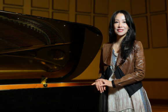 Grace Fong stands beside a grand piano in a performance hall.