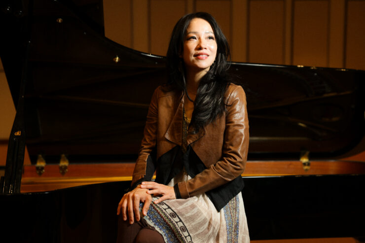Grace Fong sits beside a grand piano in a performance hall.