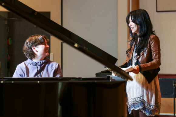 Grace Fong and student smile beside a grand piano.