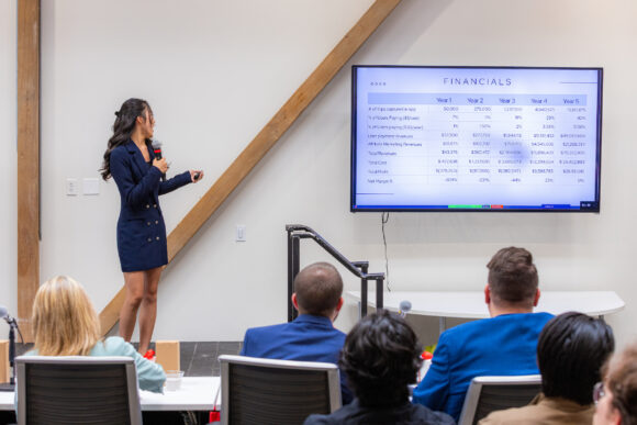 a woman presenting financial numbers to a group of seated individuals.