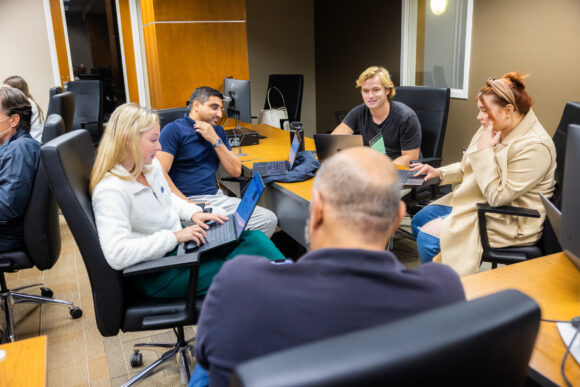 a male professor speaks with students who are gathered around a table.