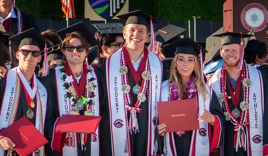 Five Chapman University graduates in caps and gowns stand together smiling on a stage at commencement. All wear "Student Athlete" stoles and medals; one holds a red Chapman University diploma cover.