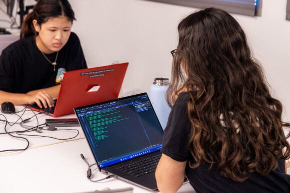 Two girls writing code using laptops