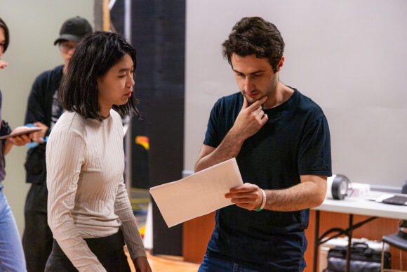 a male student is holding and looking at a script while a female student also looks at the script.