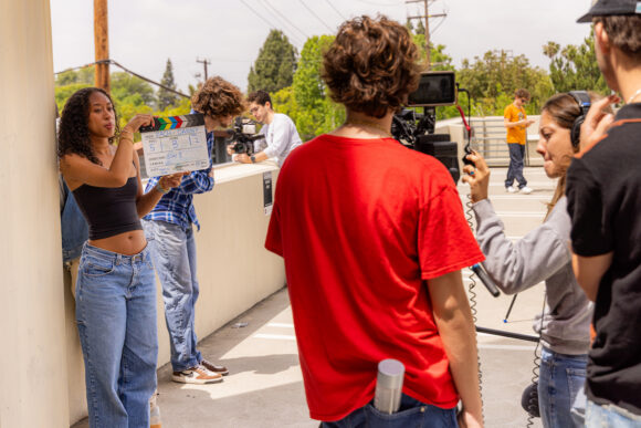 a group of students on a film set. The student closest to the camera has a script rolled up in their back pocket.