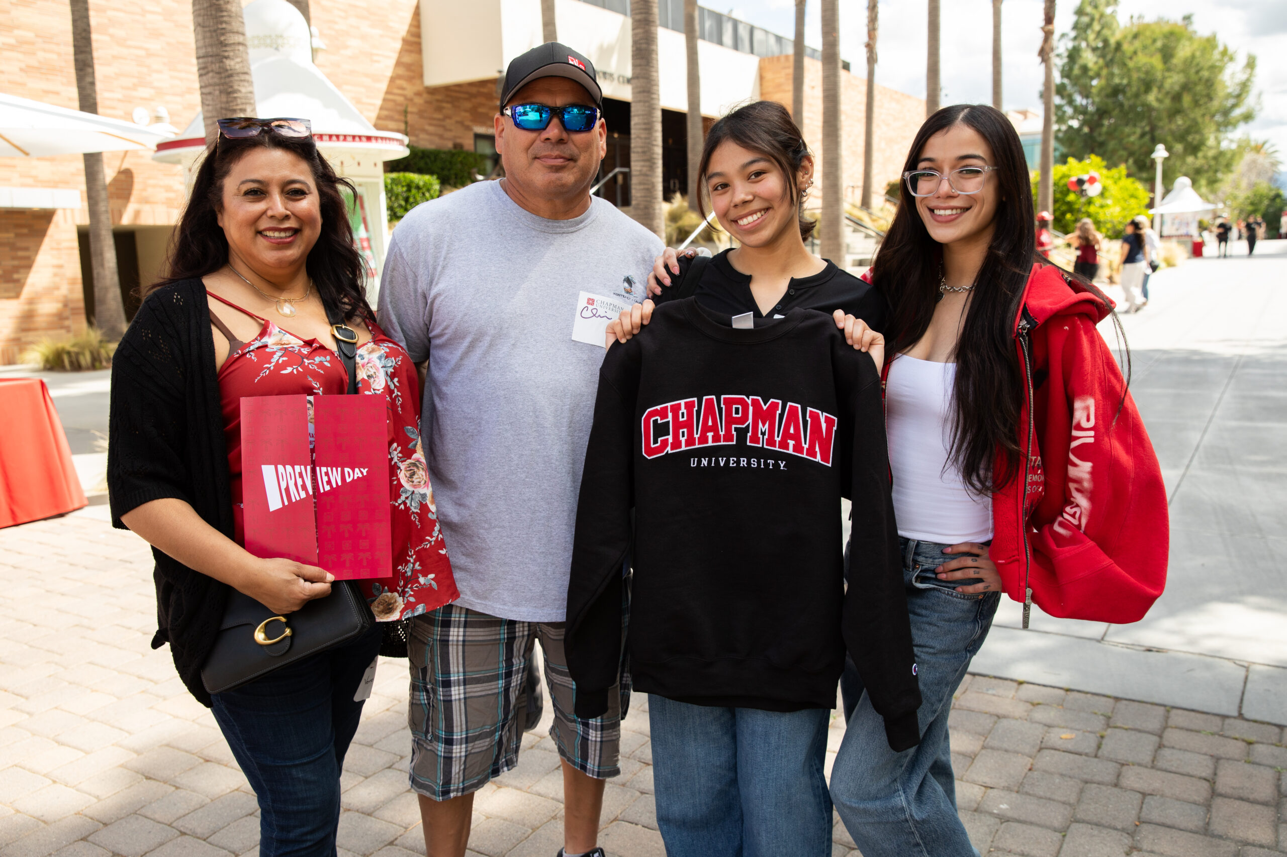 Early Action vs. Regular Decision: A student stands with their family holding up Chapman University merch on preview day
