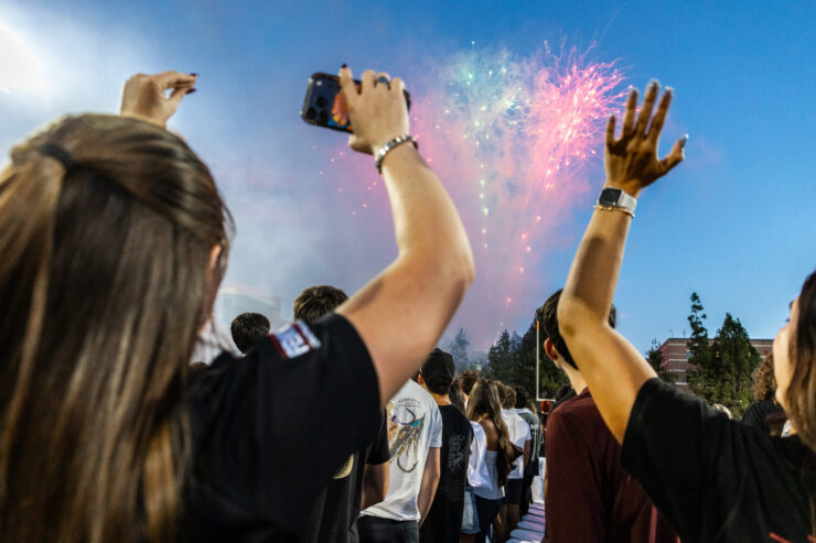 Students raise their hands and record colorful fireworks in the evening sky with a cellphone.