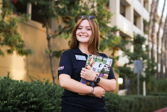 Isabel “Isa” Gomez smiles while holding a clipboard outside a Chapman residence hall on Move-In Day.
