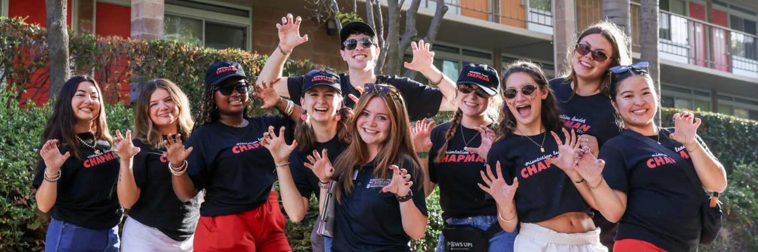 Orientation coordinator Isabel “Isa” Gomez stands at the center of a group of smiling Orientation Leaders outside a Chapman residence hall.