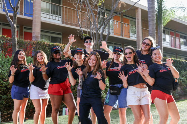 Orientation coordinator Isabel “Isa” Gomez stands at the center of a group of smiling Orientation Leaders outside a Chapman residence hall.