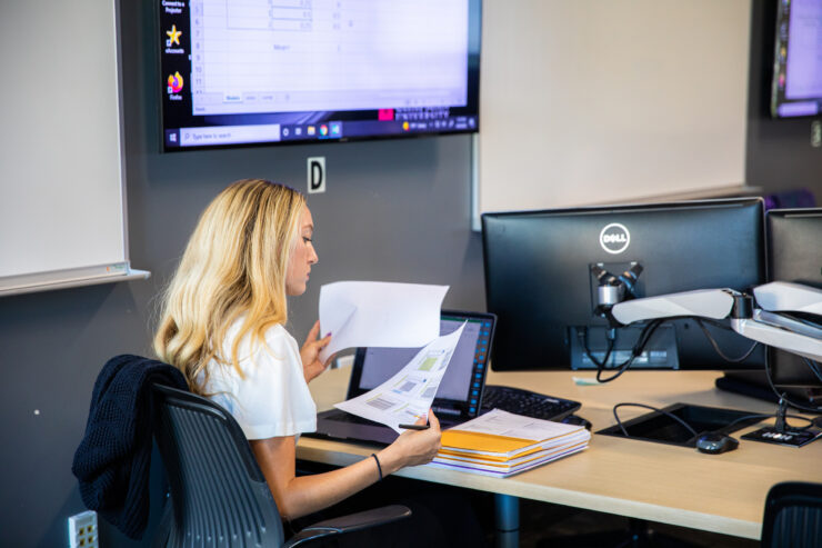 Woman reviews printed spreadsheets while working at a computer.