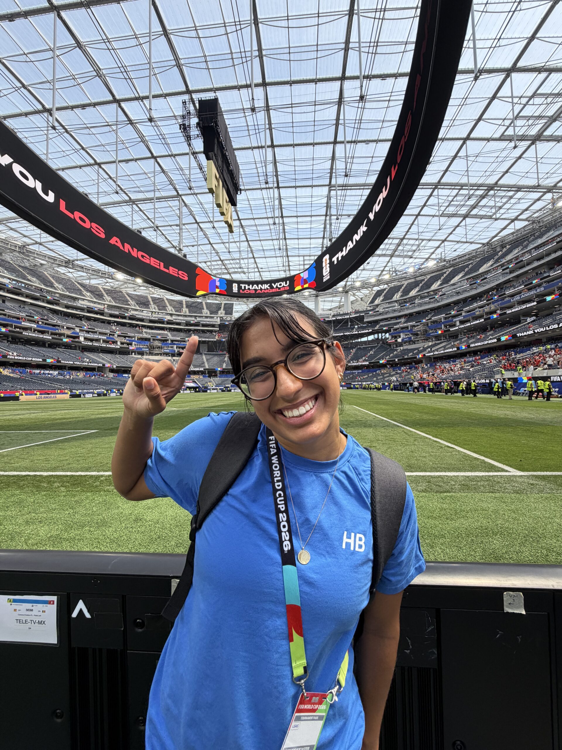Bella Ortiz smiles and raises one hand beside the field at SoFi Stadium during the FIFA World Cup.