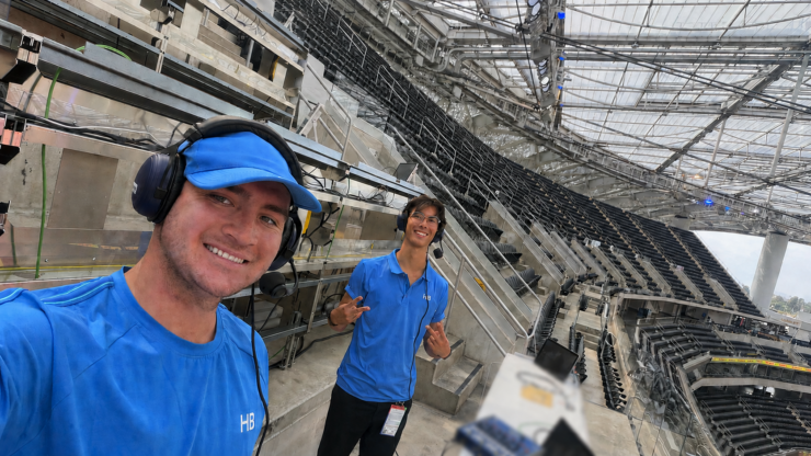 Lucas Patton and Nico Schwegler wear broadcast headphones as they pose in an empty SoFi Stadium.