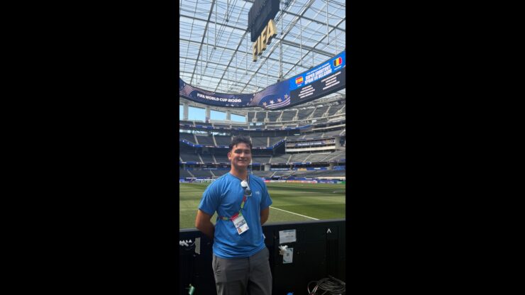 Lucas Patton smiles beside the field at SoFi Stadium beneath FIFA World Cup displays.
