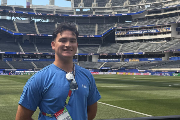 Lucas Patton smiles beside the field at SoFi Stadium beneath FIFA World Cup displays.