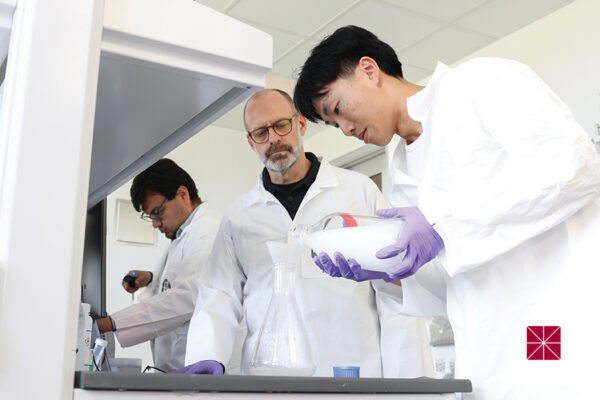 Daniel Cardenas-Vasquez, Andrew Lyon, and Ethan Ly, dressed in white lab coats, work in a lab.
