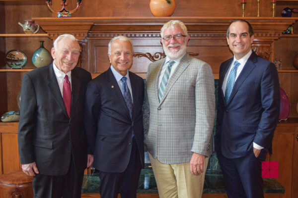 Buck Smith, Jim Doti, Daniele Struppa, and President Matt Parlow stand together in front of a wood-paneled fireplace.