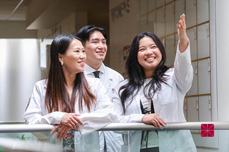 Sherry Wang, Harvey Duong, and Elena Wu are dressed in white lab coats and smiling on a balcony.